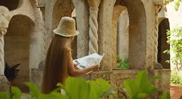 A woman in a yellow dress and straw hat explores an ancient stone...
