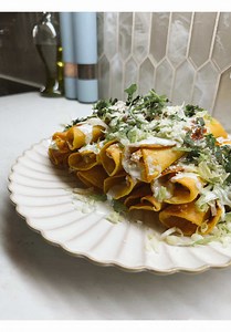 Homemade crispy golden taquitos flautas topped with crema shredded lettuce queso and cilantro