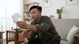 slow motion of an overjoyed chinese guy shouting with lifted clenching fist after checking winning numbers on live lottery draw in the living room at home