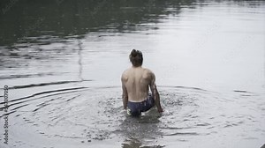 Muscled man on his back playing with water in a very cold lake