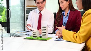 Asian real estate professionals discuss property investment plans with building models, contracts, and documents inoffice
