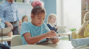 Elementary School Computer Science Class: Cute Girl Uses Digital Tablet Computer, Her Classmates work with Laptops too. Children Getting Modern Education in STEM, Playing and Learning