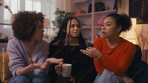 Three African American female friends gossiping and drinking tea at home party