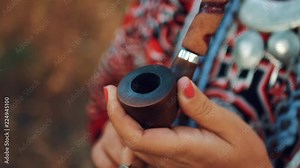 Beautiful young girl in a dress of Native Americans smoking pipe, close up