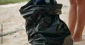Volunteers clean up trash on the beach. A close-up of a garbage bag full of plastic, into which a woman wearing gloves puts plastic bottles. Caring for the environment.