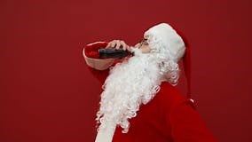 Santa Abre Una Botella De Cola Y Bebe Un Refresco Con Placer Al Fondo De Una Pared Roja. Hombre Con Traje De Santa Bebe Cola Metrajes - Vídeo: 201089538