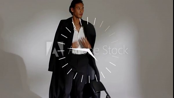 Vertical video: Male model swinging coat open on fashion set, draping and timing poses to clock