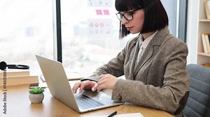 Confident young employee in formal wear unlocking laptop keyboard with password at desk in modern office. Caucasian female worker investigating trademarks using search engine in creative workplace.