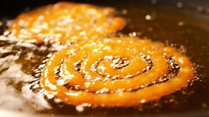 Download Preparing traditional Indian Jalebi sweet dessert. A close-up of the spiral funnel cake frying in hot, bubbling, sizzling oil for free
