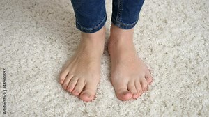 Closeup of barefoot woman in jeans standing on soft white carpet and moving toes