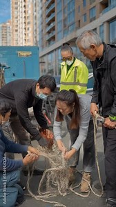 Group of adults wearing masks repair fishing net outside apartment building on sunny day, community activity, working collaboratively, and fixing nets
