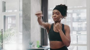 Serious african amerian athletic woman punching the air with her fists training warm-up before boxing workout at home interior. Sports. Activity. Motivation. Confidence.