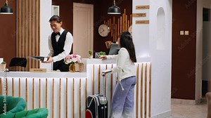 Asian hotel guest asking receptionist about amenities upon her arrival at five star resort, showing her room reservation at front desk. Concierge greeting woman with luggage, tourism concept. Stock Video