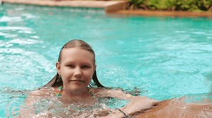 Teenage girl carefully climbing out of a swimming pool with wet hair and swimsuit.