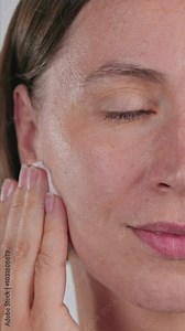 Vertical Screen: Closeup half-face Gorgeous Caucasian woman use Cotton Round, applying toner, cleansing face, removing makeup. Young woman gently rubs a cotton pad on cheek, cleanses the skin.