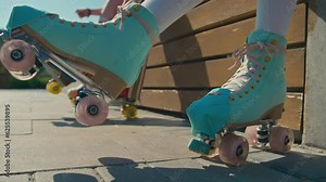 Ground level close up of legs of unrecognizable girls sitting on bench in park on sunny summer day wiggling legs and checking quad skates before riding