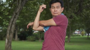 Asian mature man doing arm shoulder muscle stretching before exercise Inside public park with trees and green grass, morning exercising routine, active Motivation after retirement life, body condition