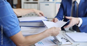 business man and woman are sitting at the table and sorting documents with a stapler