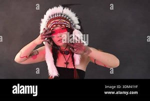 Shaman woman in native American Indian headdress with face painting and dreamcatchers performing ritual on dark background with smoke