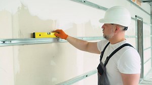 A man builder measures of the horizontal deviation of plasterboard wall