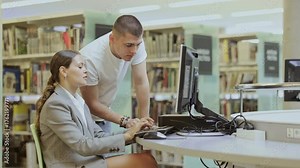 In reading room, girl student works on computer under guidance of male teacher, searches for information online, checks and analyzes public data, student creates essay and completes homework Stock Video