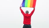 L’homme lever arc-en-ciel couleur LGBTI drapeau ondulant dans le vent...