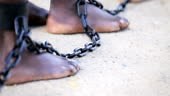 Slaves feet shackled together as they walk along slowly.