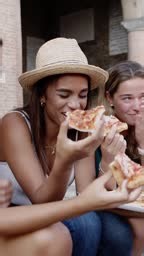 Three happy young multiracial women eating pizza in the street