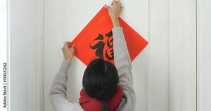 Woman sticking chinese calligraphy on door at home, chinese calligraphy word meaning luck