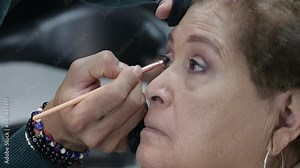 Eyeliner on an older Mexican model in a professional makeup session, senior granny with short brown hair and tanned skin. Old age fashion, beauty and makeup concept