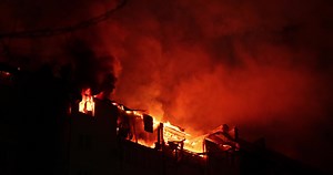 Huge fire blazing in apartment building. Burning house is engulfed in flames at night during the disastrous