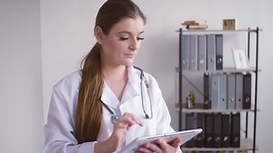 Redhead doctor woman in white coat using a tablet and looking at the camera | Free Stock Video Footage