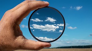 Visual effect of the polarizing filter on the example of a summer rural landscape with beautiful clouds. The hand holds a circular filter, applying the polarization effect. | Premium Stock Video Footage
