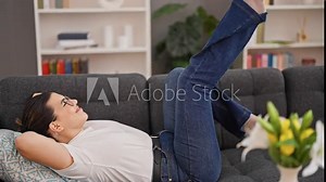 Young beautiful hispanic woman excited lying on sofa moving legs in the air at home