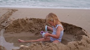 Cute laughing blonde three years old girl playing with sand at beach near sea in Spain.Child activity, happiness.Kid having fun at resort on vacation.