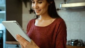 Attractive woman using tablet device, reading recipe while cooking on her kitchen. Close up