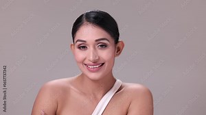 A beautiful young woman with clean, fresh skin stands gracefully against a light grey background, radiating natural beauty. High quality 4k footage.