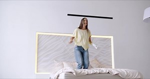 Happy girl with bionic arm jumping on bed at home, woman with disability having fun, rasing prosthetic arm while enjoy time alone at home, artificial prosthetic limb