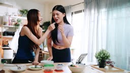 Two women cooking together and playfully feeding each other healthy...