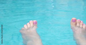 Female feet in swimming pool. Female wave her feet in blue water.