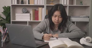 Teenage Asian woman, feeling bored, rests asleep beside the bookcase filled with academic textbooks, her mind drifting away from the assignment course on campus. learning and depression.