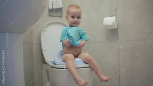 child toddler baby sitting toilet lavatory seat smiling looking camera hygiene education kid pee potty seat. concept healthy children. little child boy wc closet poop. caucasian baby blue shirt sit