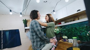 A couple embraces in their cozy camper kitchen, sharing a warm, intimate moment filled with love during their journey.