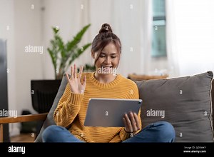 Happy smiling asian young woman in yellow sweater with tablet pc computer having video call and waving hand at home Stock Photo - Alamy