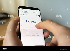 A man's hand holding an Android smartphone at home and selecting the Google Search bar on the google.com search engine homepage Stock Photo - Alamy