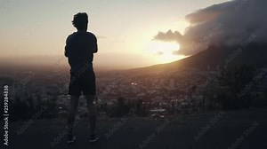 Full body shot of a young white male stretching his body and overlooking the city and nature outdoors