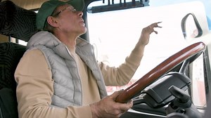 Free stock video - Bottom view of older worker wearing cap and vest driving a truck in a logistics park