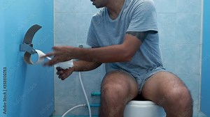 Young asien man retrieves some toilet paper to use after defecate In the bathroom