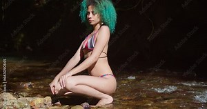 A woman in a bikini squats at the river edge on a tropical island in the Caribbean