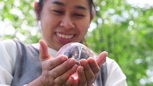 Download Portrait of Asian woman holding crystal ball in hand and wishing on green nature background. for free